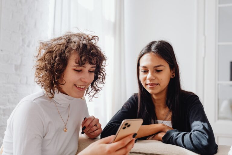 Two young women enjoying a moment together indoors while sharing content on a smartphone.