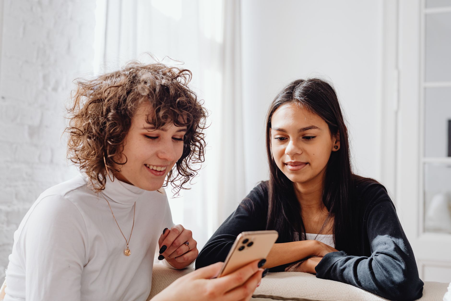 Two young women enjoying a moment together indoors while sharing content on a smartphone.