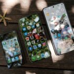 A collection of smartphones showing different app icons, placed on a wooden surface in natural light.