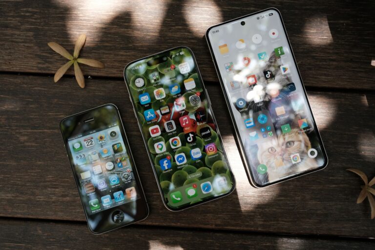 A collection of smartphones showing different app icons, placed on a wooden surface in natural light.
