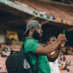 A man in a green shirt capturing moments at a lively sports stadium.