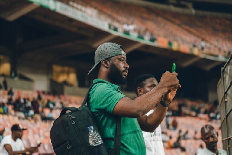 A man in a green shirt capturing moments at a lively sports stadium.