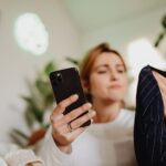 A woman uses her smartphone indoors for online shopping, holding fabric.