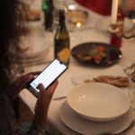 A cozy dinner setting with a woman using a smartphone at a candlelit table.