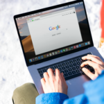 Individual typing on a laptop outdoors with snow, accessing the internet.